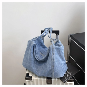 Detailed view of light blue denim tote bag with metal eyelet strap on white suitcase
