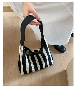 Detailed close-up of striped knit hobo bag featuring black leather handle and woven texture