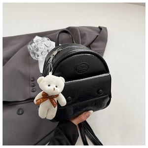 Detail of a mini black faux leather backpack featuring a cute white plush bear charm