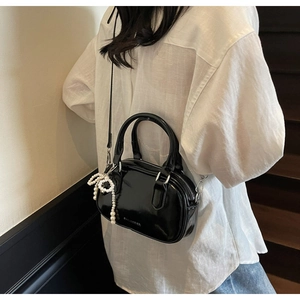 Detail of black glossy leather pillow bag with pearl bow charm on casual outfit