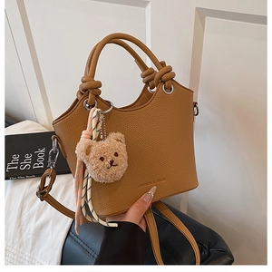 Detail of brown litchi leather bucket bag with knotted handle and plush bear charm