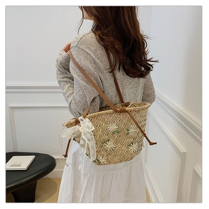 Detail of straw bucket bag featuring white daisy embroidery and a white lace bow knot