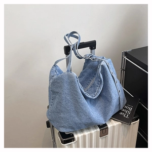 Close-up of blue denim tote bag with metal eyelet details on a white suitcase