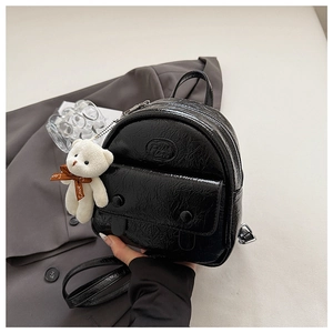 Detail of black patent leather mini backpack with pleated texture and plush bear charm