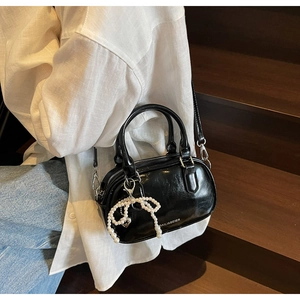 Detail of black oil wax leather boston bag featuring pearl bow and brand lettering