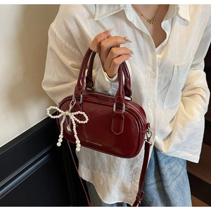 Detail of burgundy oil wax leather Boston bag with pearl bow charm and top handle