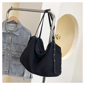 Detail view of a large black canvas tote bag with metal eyelets hanging on a silver rack