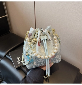 Détail du sac seau en brocart bleu clair avec broderie papillon et poignée en perles