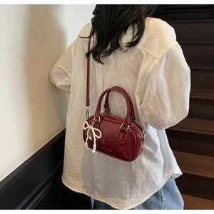 Detail view of burgundy oil wax leather Boston bag with a pearl bow charm and strap