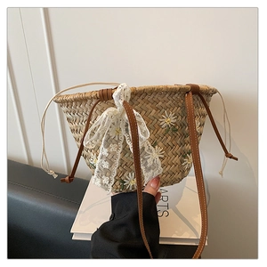 Detail of straw bucket bag featuring daisy embroidery and a white lace bow accent