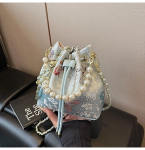 Détail du sac seau brodé bleu clair avec poignée en perles et bandoulière chaîne