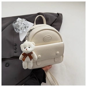 Detail of creamy white textured mini backpack with a cute plush bear charm on a suit