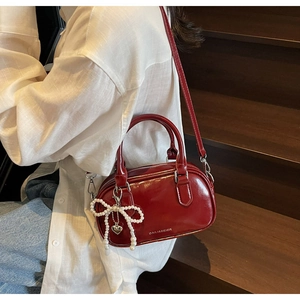 Detail of red oil wax leather pillow bag with pearl bow charm and metal logo lettering