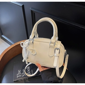 Detail view of a white vintage oil wax leather Boston bag with pearl bow charm on a book