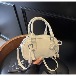 Detailed macro view of cream Boston bag with pearl bow charm and silver metallic branding
