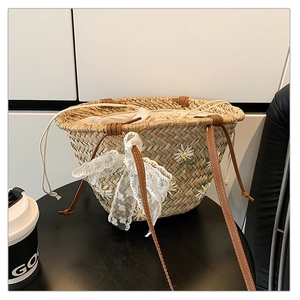 Detail of straw bucket bag with daisy embroidery, lace bow, and leather strap