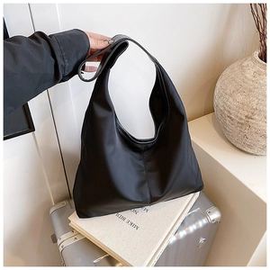 Detail of a black hobo bag with a vertical seam and wide shoulder strap in home setting