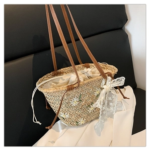 Detail view of woven straw bucket bag with floral embroidery and white lace bow decoration