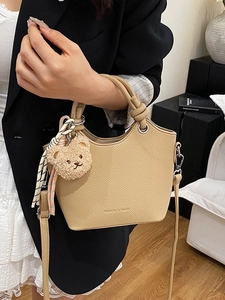 Fashionable beige bucket bag in pebble leather with plush bear charm and striped ribbon