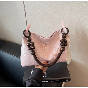 Détail du sac rose avec broderie papillon, poignées en perles de bois et gland