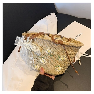 Close-up of straw bucket bag featuring daisy embroidery and a white lace bow detail
