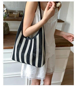 Detail of black and white striped knit tote bag featuring a textured weave and leather strap