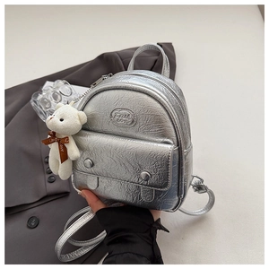 Detail of silver metallic mini backpack with plush bear charm and fashion logo patch