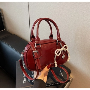 Detailed shot of burgundy faux leather handbag featuring a pearl bow and heart charm