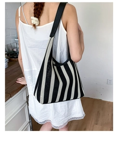 Close-up of a striped knit tote bag with black leather straps on a model's shoulder
