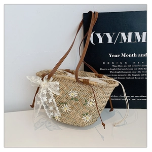 Detail of hand-woven straw bucket bag with white daisy embroidery and lace bow