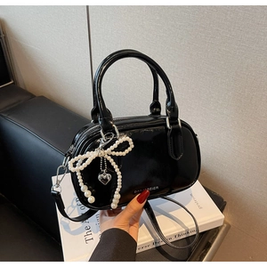 Detail of a shiny black oil-wax leather satchel with a pearl bow and heart charm