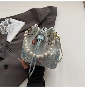 Détails de broderies de nuages et papillons sur sac seau en satin bleu clair