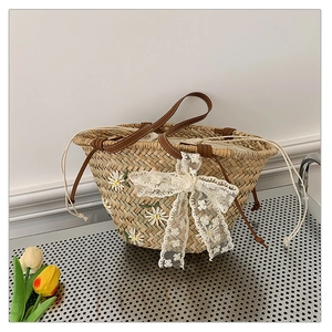 Detail of straw bucket bag featuring daisy embroidery and a white lace bow decoration