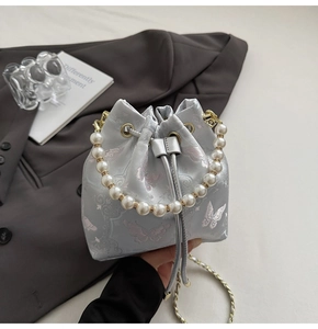 Détail du sac seau brodé bleu clair avec anse en perles et motif papillon rose