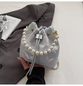 Détail de broderie papillon rose et poignée en perles sur un sac seau en soie bleue