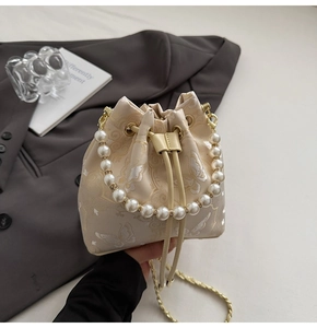 Détails de broderie sur sac seau crème avec poignée perle et bandoulière dorée