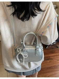 Silver metallic Boston bag with pearl bow charm and heart tag shown on model
