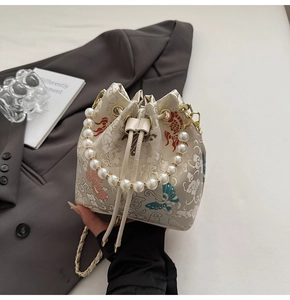 Détail de broderie sur sac seau crème avec poignée en perles et chaîne dorée