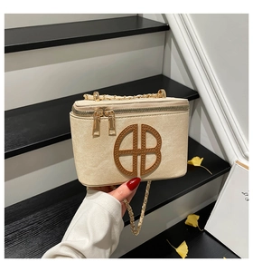 Detail showing the brown leather monogram logo and woven chain strap on a cream bag