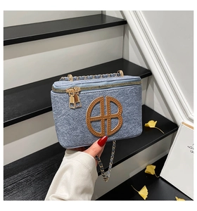 Close-up of light blue denim tote bag with golden circular AB logo and chain strap