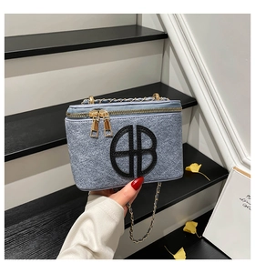 Detail of light blue tweed box bag featuring black logo and gold chain strap