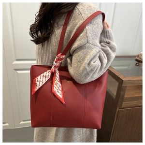 Detail of red minimalist tote bag with gold logo and decorative silk scarf on the strap