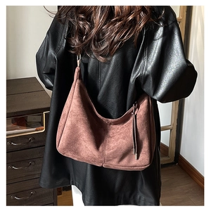 Brown suede crescent tote bag with fringe detail worn with a black leather jacket