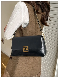 Detail of black shoulder bag featuring textured paneling and golden interlocking buckle