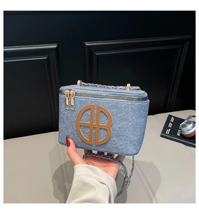Détail du sac carré en tweed bleu clair avec logo AB en cuir brun et chaîne dorée