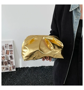Détail de la pochette plissée dorée à texture métallique tenue à la main pour soirée