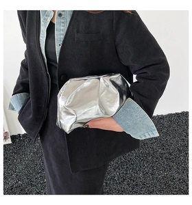 Detail shot of a shiny silver pleated cloud clutch bag held by a person in black coat