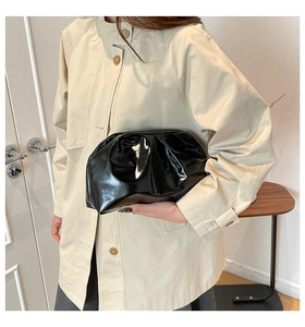 Detail of a black patent leather pleated clutch bag held by a model in a beige coat
