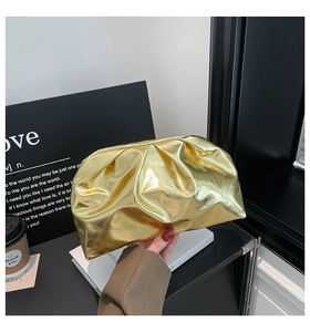 Détail d'une pochette de soirée plissée dorée tenue sur un fond minimaliste chic