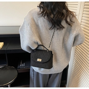 Quilted black suede crossbody bag with gold twist lock and chain strap on a model